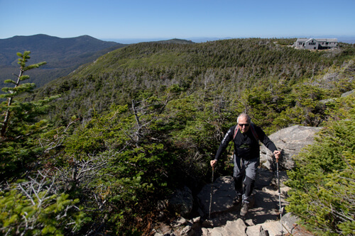 A man hiking up the Franconia Ridge Trail on Mount Lafayette. You can see a mountain hut in the background.