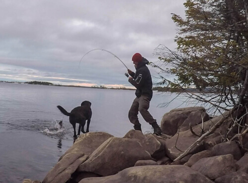 Justin Barbour, The Newfoundland explorer, catching a fish while his dog Saku await for dinner